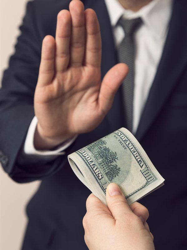 A businessperson raising a hand to refuse folded cash offered by another hand