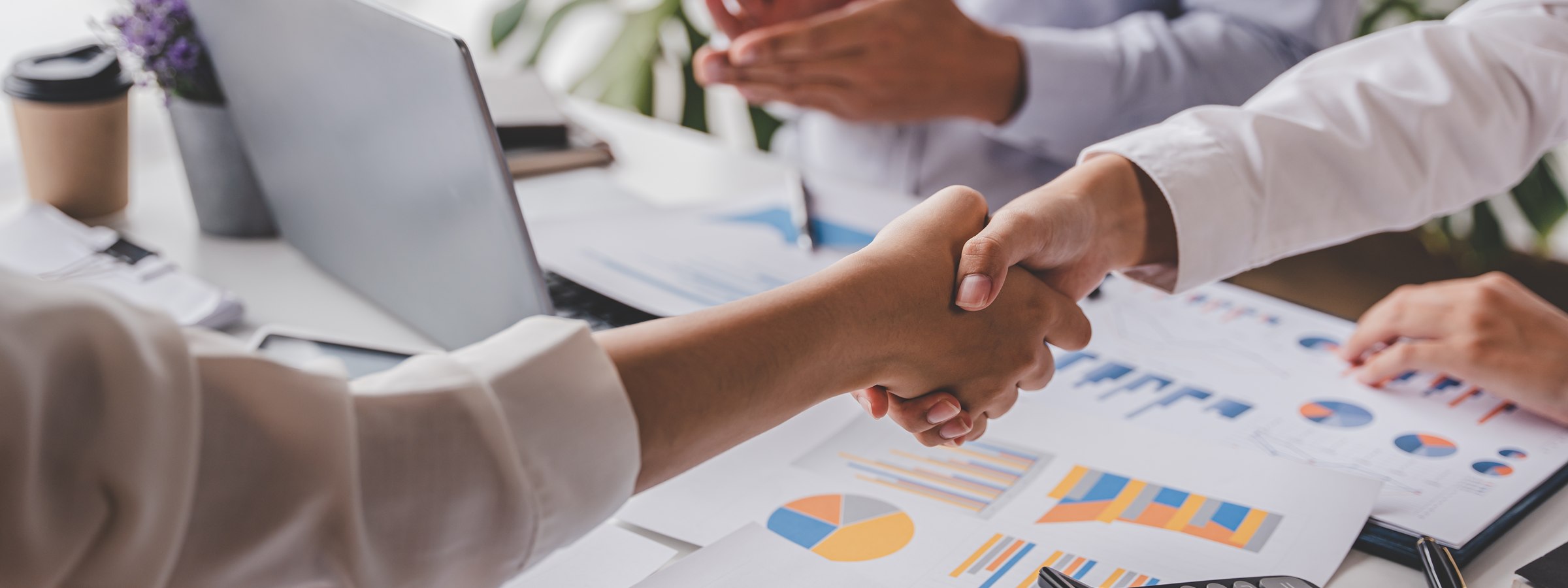 Two insurance professionals shaking hands over financial charts and a laptop